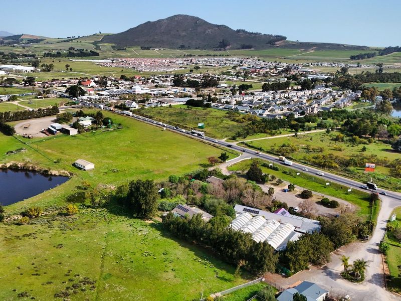 Aerial view of the commercial property featuring a greenhouse structure, solar panels, and surrounding land with a dam and road access.