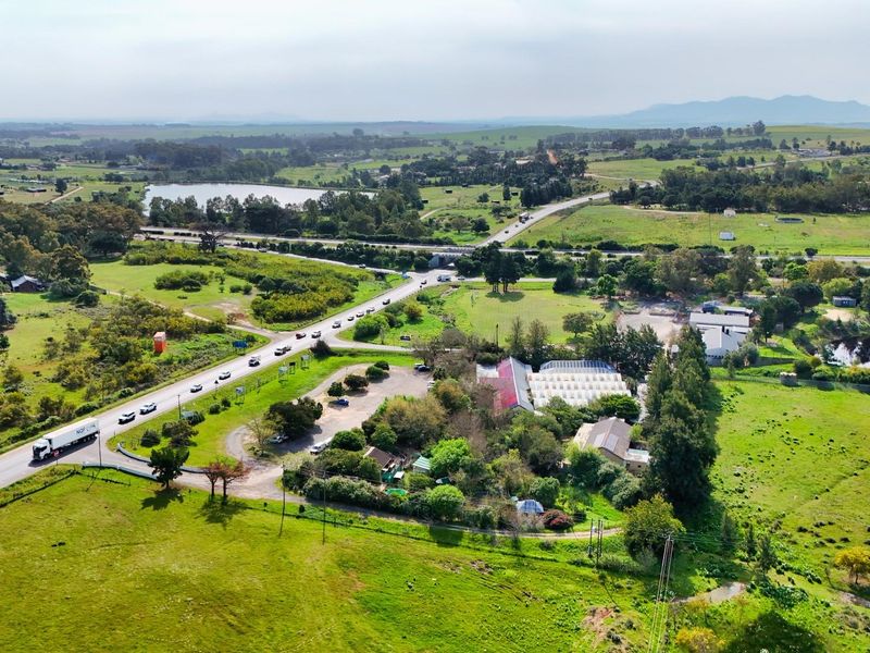 Aerial view of a commercial property featuring greenhouse structures, a paved parking area, and direct access to a main road in a rural setting.