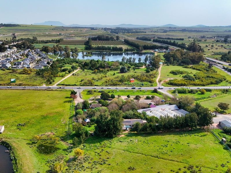 Aerial view of a commercial property featuring multiple structures, solar installations, and surrounding green space with access to main road infrastructure.