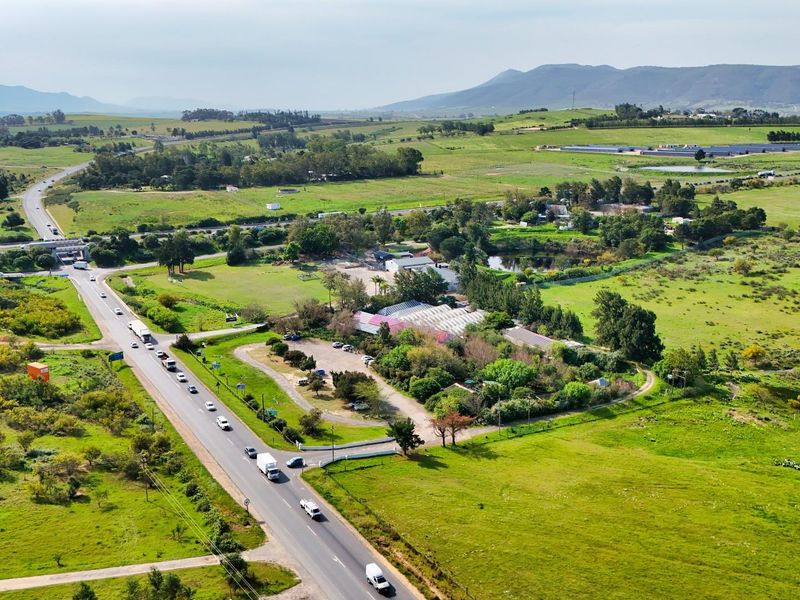 Aerial view of a commercial property situated on a large rural plot with direct access to a main road and surrounding natural landscape.