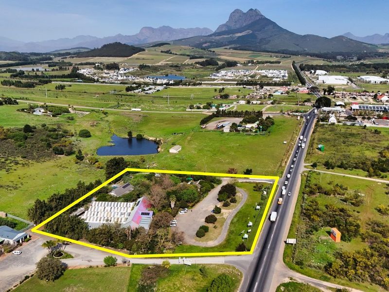 Aerial view of a commercial property featuring a large building, paved parking area, and landscaped grounds, situated with convenient road access.