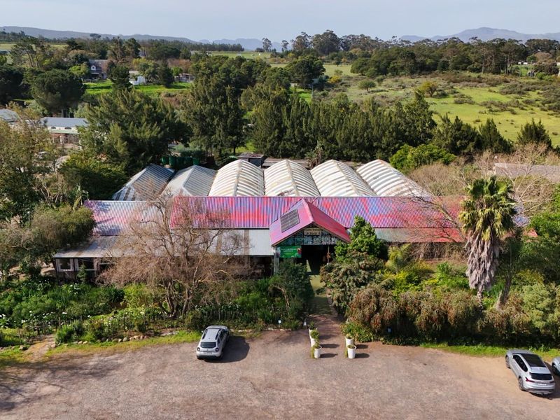 Aerial view of a commercial property featuring a large greenhouse-style structure with corrugated metal roofing, surrounded by landscaped grounds and a gravel parking area.