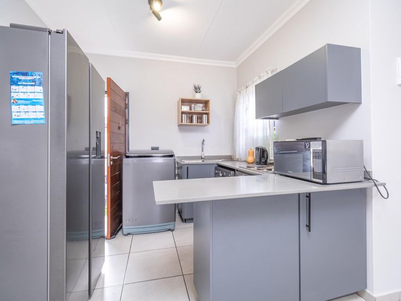 A functional scullery featuring modern grey cabinetry, stone countertops, a stainless steel sink, and tiled flooring, providing additional workspace and utility.