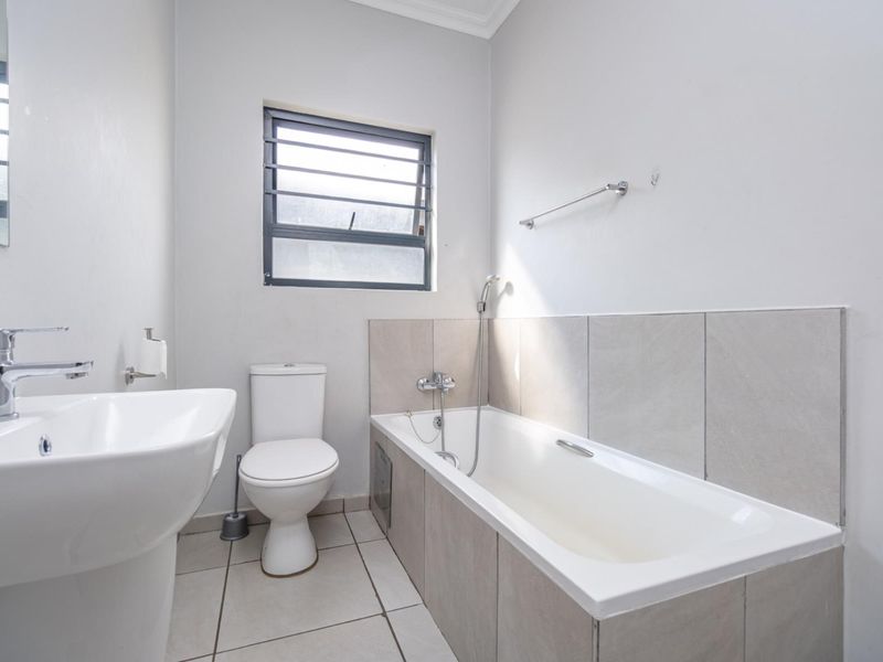A clean and functional bathroom featuring a pedestal basin, toilet, and a tiled bathtub with a handheld shower attachment.