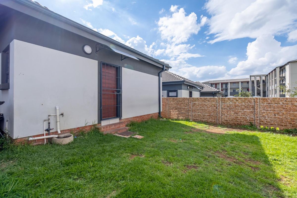 A rear exterior view of the property featuring a small private garden, a security gate, and a perimeter precast concrete wall.
