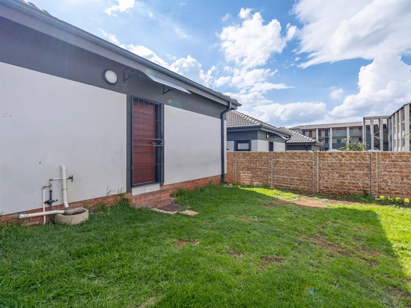 A rear exterior view of the property featuring a small private garden, a security gate, and a perimeter precast concrete wall.