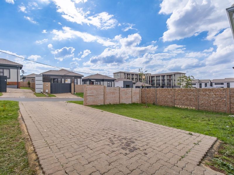 A view of the property frontage featuring a paved driveway, lawn area, and a combination of precast concrete and stone-clad boundary walls.