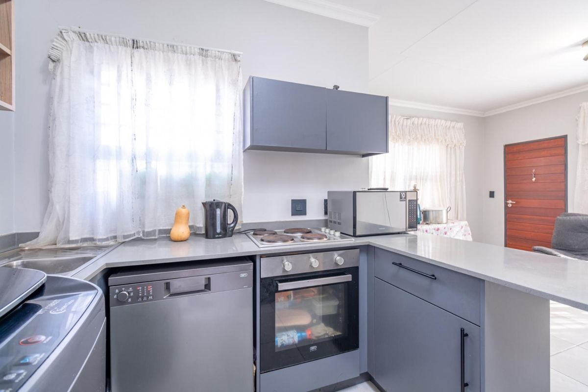 A functional kitchen featuring modern grey cabinetry, stone countertops, a built-in oven, and an electric hob, providing a clean and efficient workspace.