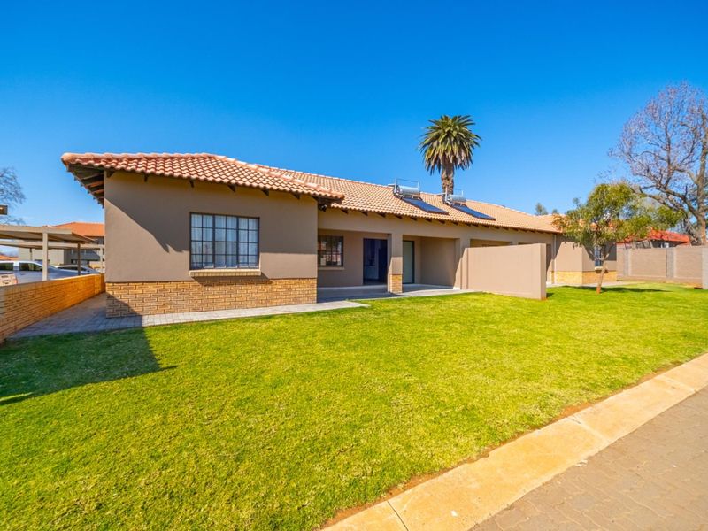A well-maintained single-story house exterior featuring a terracotta tiled roof, solar water heating system, brick accents, and a neat front lawn.