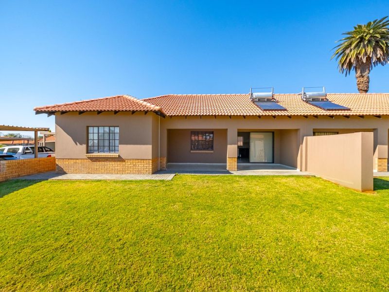 Rear view of the property featuring a covered patio, well-maintained lawn, and a solar water heating system installed on the tiled roof.