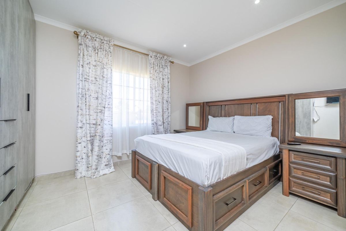 A well-maintained bedroom featuring neutral tiled flooring, recessed downlighting, and a large built-in wardrobe for ample storage.