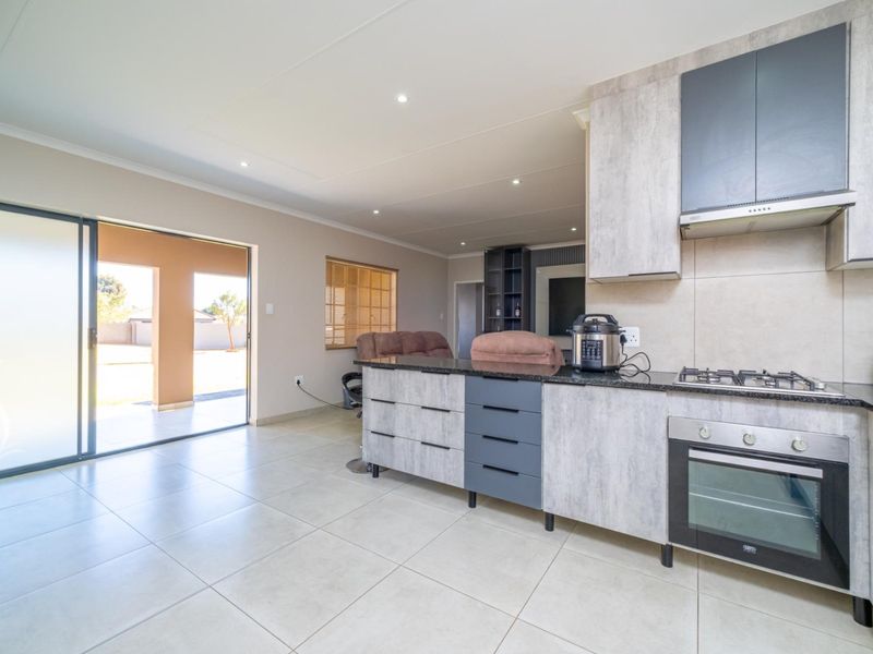 Modern open-plan kitchen featuring granite countertops, built-in oven, gas hob, and extractor fan, seamlessly flowing to an outdoor patio through sliding glass doors.