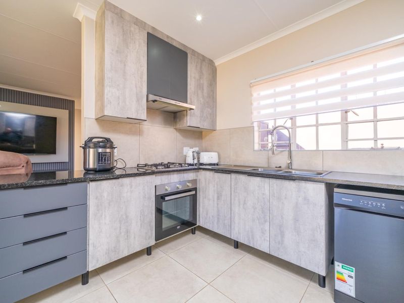 Modern kitchen featuring grey wood-look cabinetry, granite countertops, built-in oven, gas hob, and a double sink with tiled finishes.