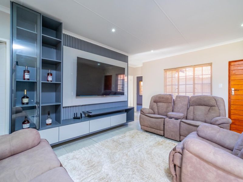 A modern living room featuring a custom built-in media unit with integrated shelving, slatted wall paneling, and neutral tiled flooring.