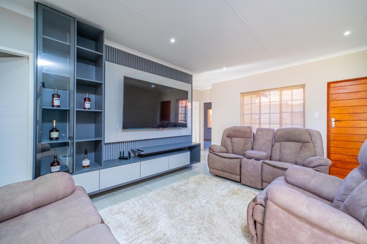 A modern living room featuring a custom built-in media unit with integrated shelving, slatted wall paneling, and neutral tiled flooring.