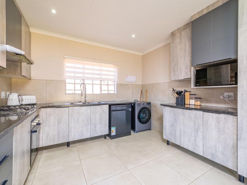 Modern kitchen featuring grey wood-look cabinetry, granite countertops, gas hob, extractor fan, and integrated space for appliances with neutral tiled flooring.