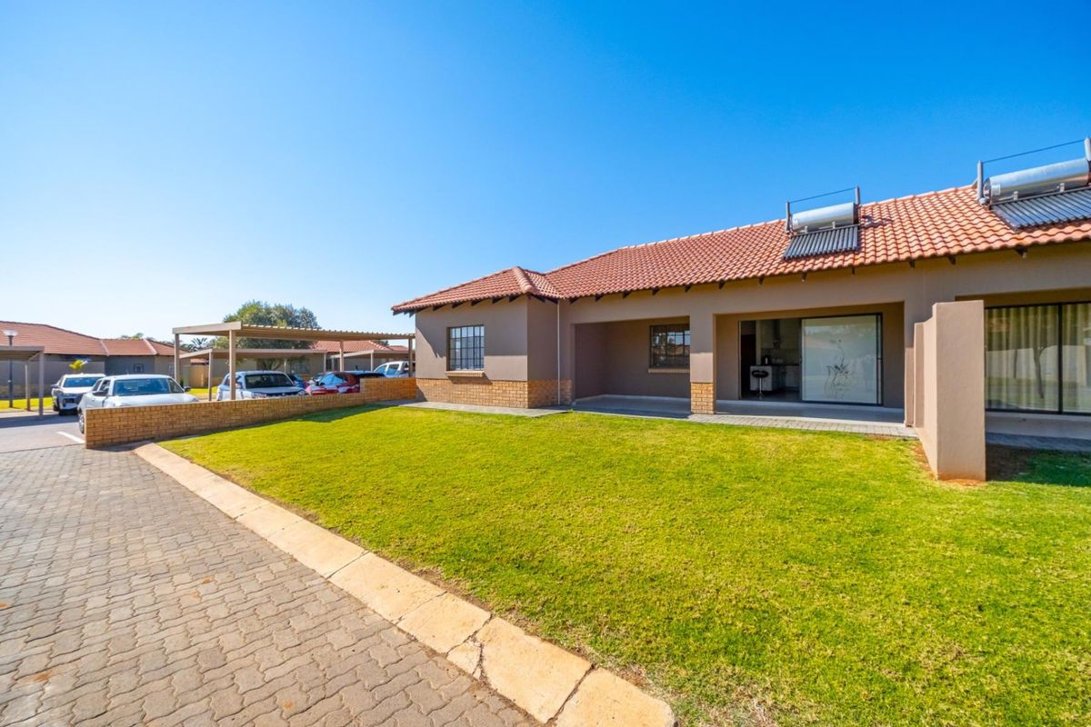 Rear view of the property featuring a lawn, covered patio, paved driveway, and solar water heating system installed on the tiled roof.