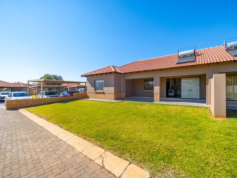 Rear view of the property featuring a lawn, covered patio, paved driveway, and solar water heating system installed on the tiled roof.