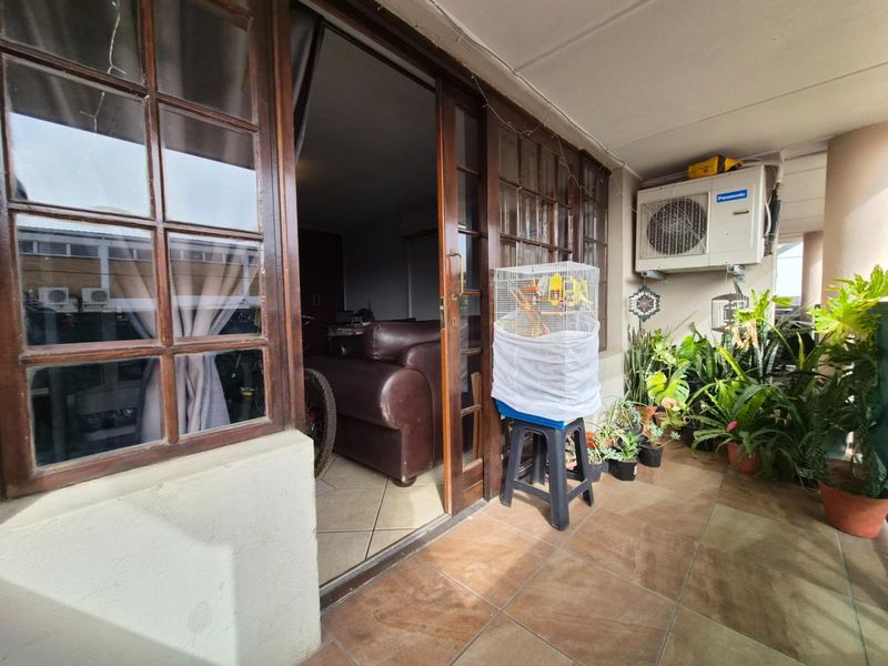 A covered balcony featuring tiled flooring and wooden sliding doors, providing a transition space between the interior living area and the outdoors.