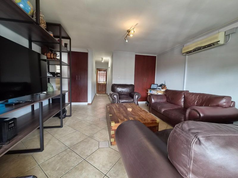 Spacious living room featuring tiled flooring, built-in storage cupboards, and a wall-mounted air conditioning unit.