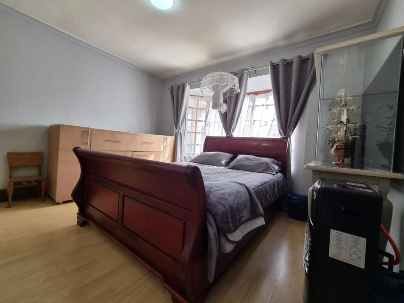 A bedroom featuring light-toned laminate flooring, neutral wall paint, and a window with curtain treatments.