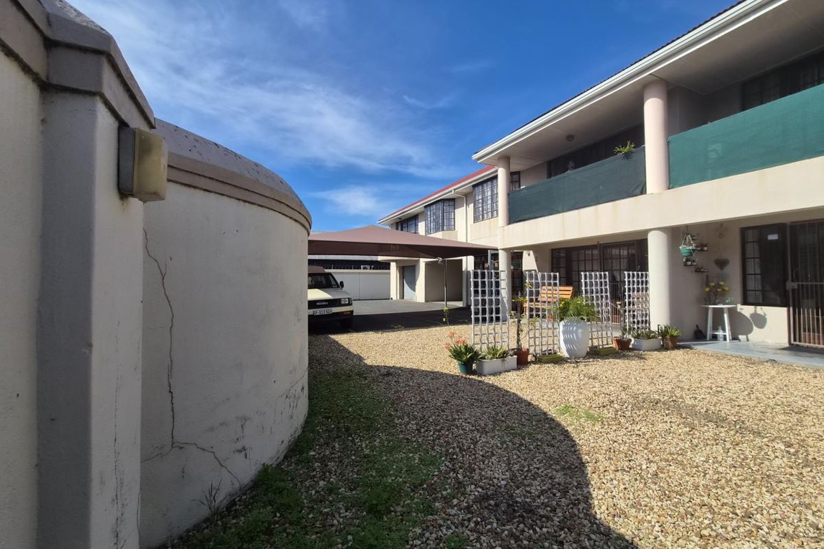 Rear exterior view of the apartment complex featuring a gravel courtyard, covered carport parking, and upper-level balcony access.
