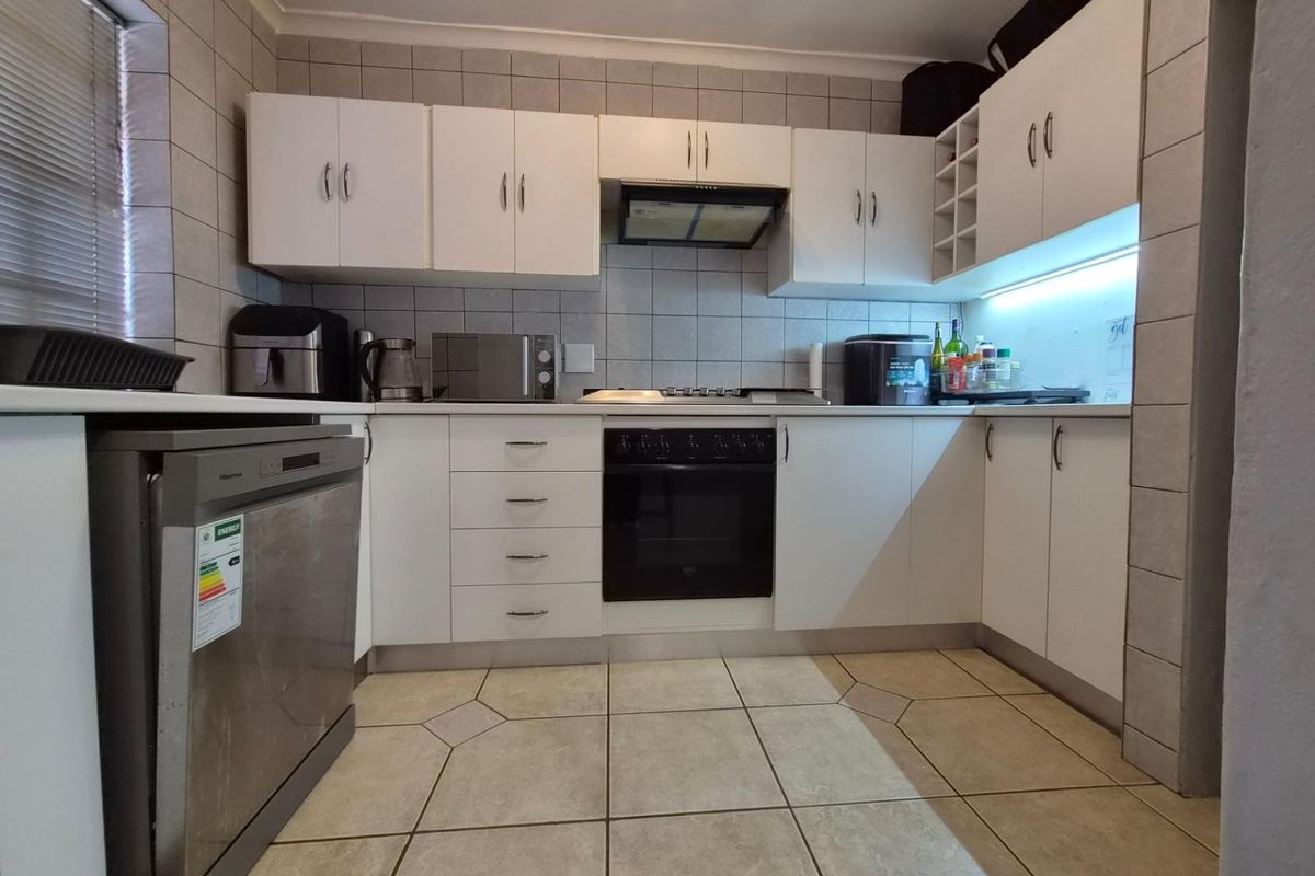 A functional kitchen featuring white built-in cabinetry, a tiled splashback, integrated oven and hob, and tiled flooring with under-cabinet lighting.