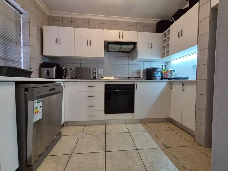 A functional kitchen featuring white built-in cabinetry, a tiled splashback, integrated oven and hob, and tiled flooring with under-cabinet lighting.