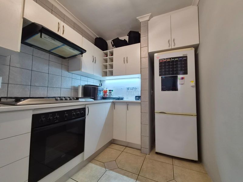 A functional kitchen featuring white built-in cabinetry, a gas hob with extractor fan, oven, and tiled finishes throughout.
