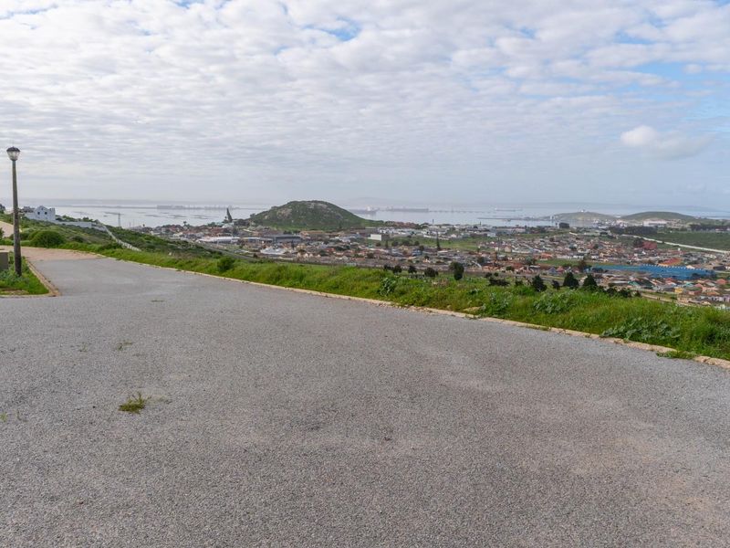 Elevated view overlooking the surrounding residential area and distant coastline from a paved access road.