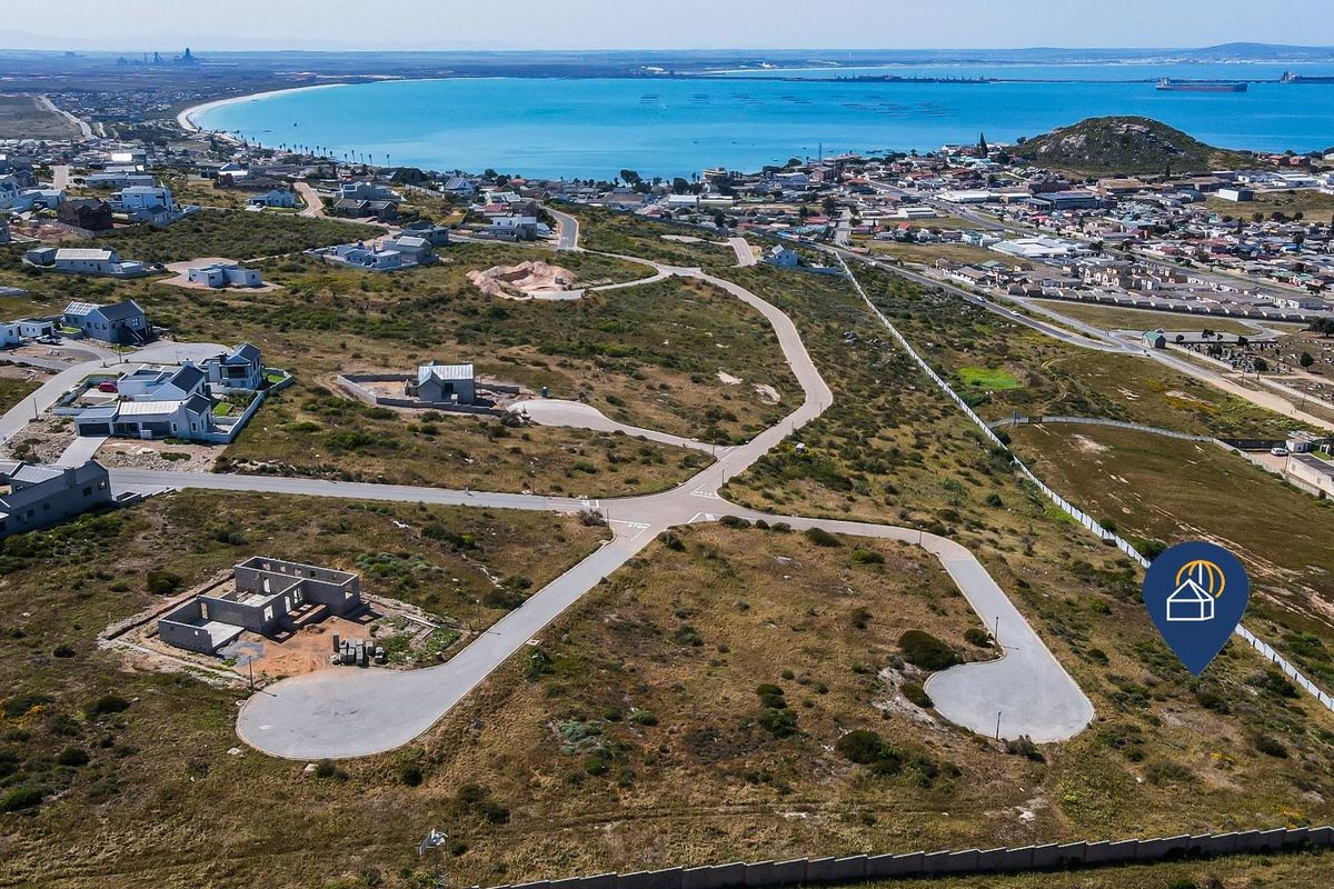 Aerial view of a residential development site featuring paved roads and coastal proximity, showcasing the surrounding neighborhood and ocean views.