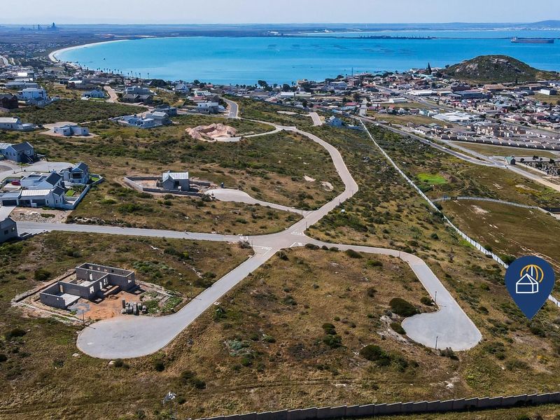 Aerial view of a residential development site featuring paved roads and coastal proximity, showcasing the surrounding neighborhood and ocean views.