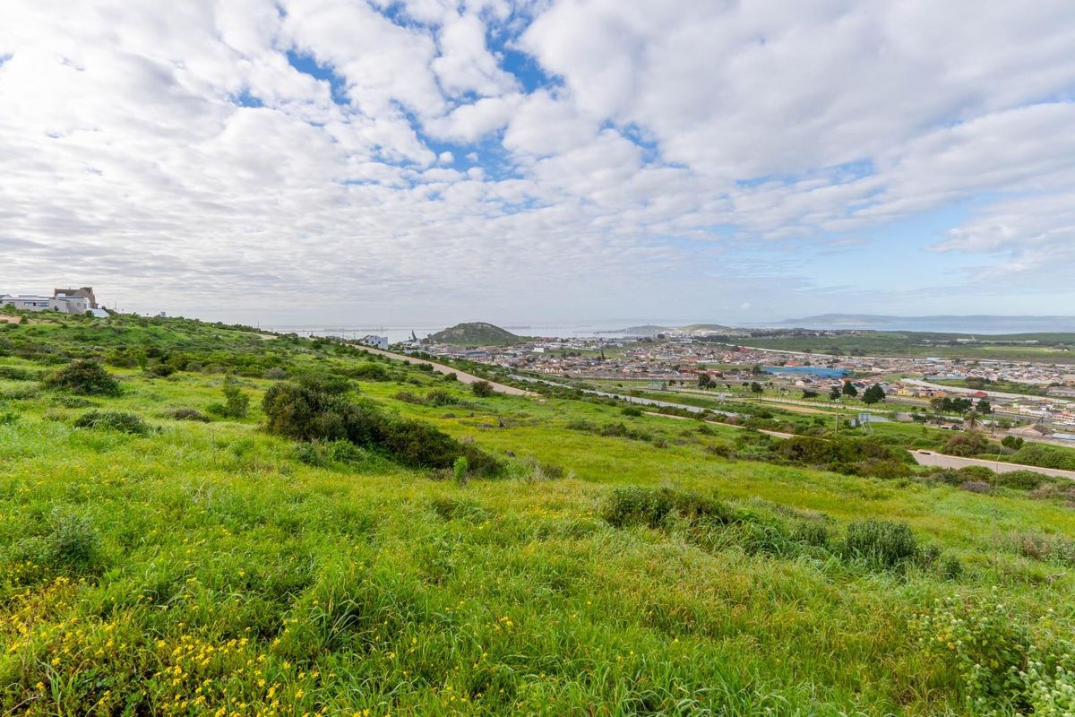 A wide-angle view of the surrounding landscape, showing the sloping vacant land with distant town and coastal scenery.
