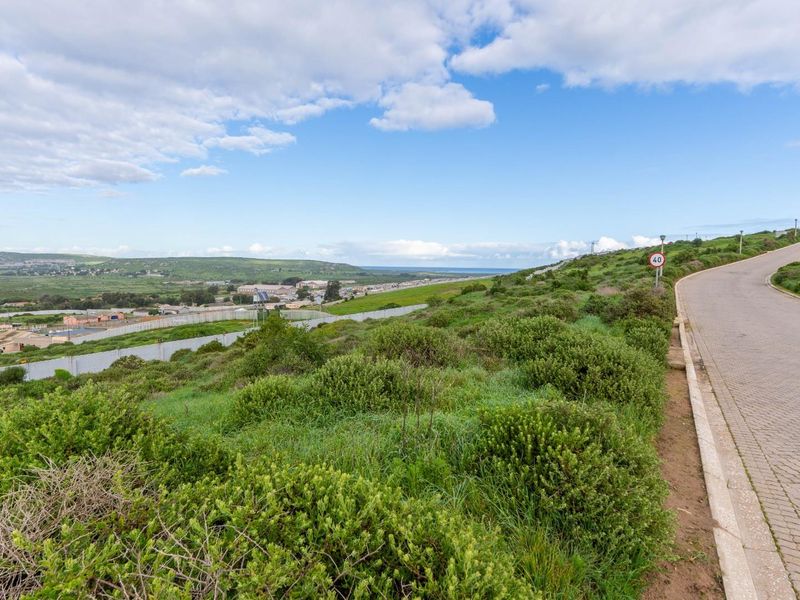 A scenic view overlooking a residential area and landscape, featuring a paved road and boundary wall on a vacant residential plot.