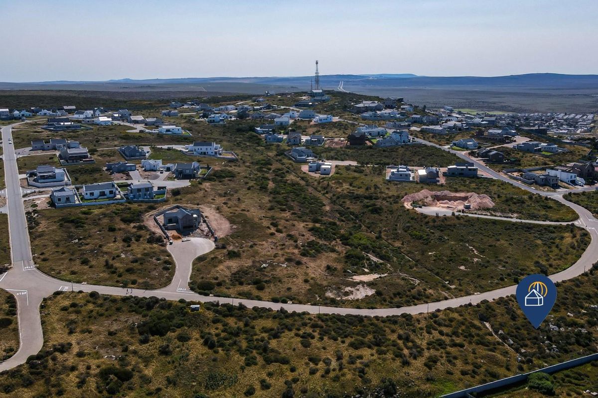 An aerial view of a residential estate development featuring paved roads and multiple vacant plots set within a natural coastal landscape.