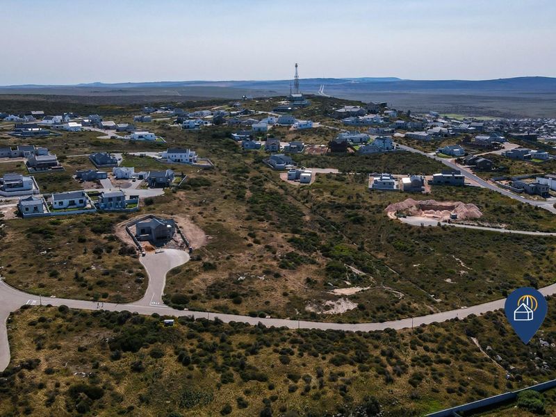 An aerial view of a residential estate development featuring paved roads and multiple vacant plots set within a natural coastal landscape.