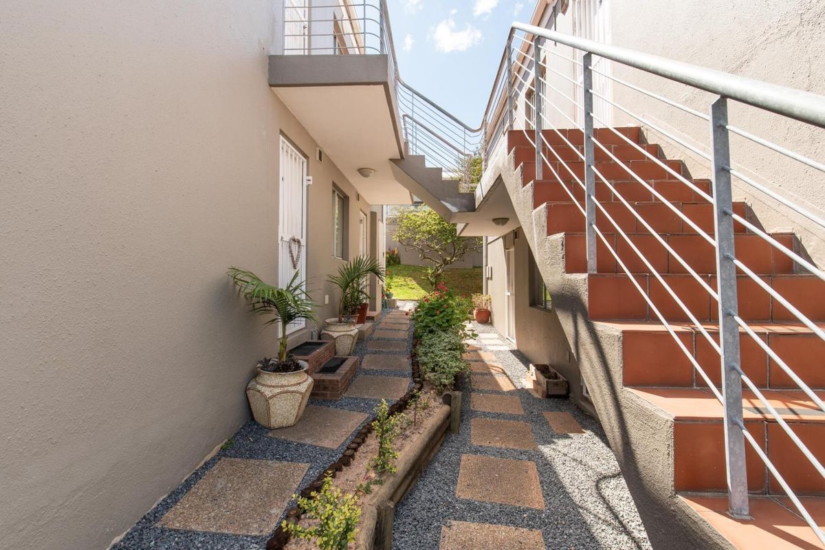 Exterior view of an apartment complex featuring a paved walkway, landscaped garden beds, and an external staircase with metal railings.