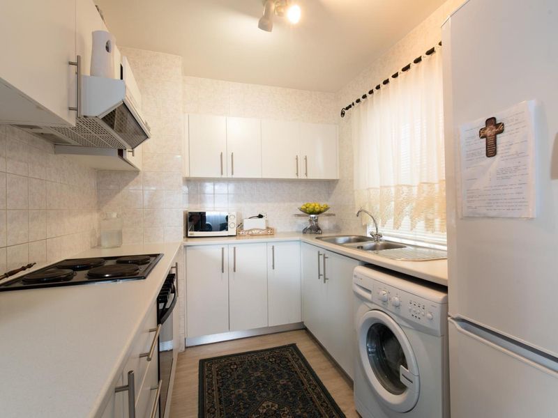 A functional galley-style kitchen featuring white cabinetry, tiled backsplash, integrated electric hob, oven, and dedicated space for laundry appliances.