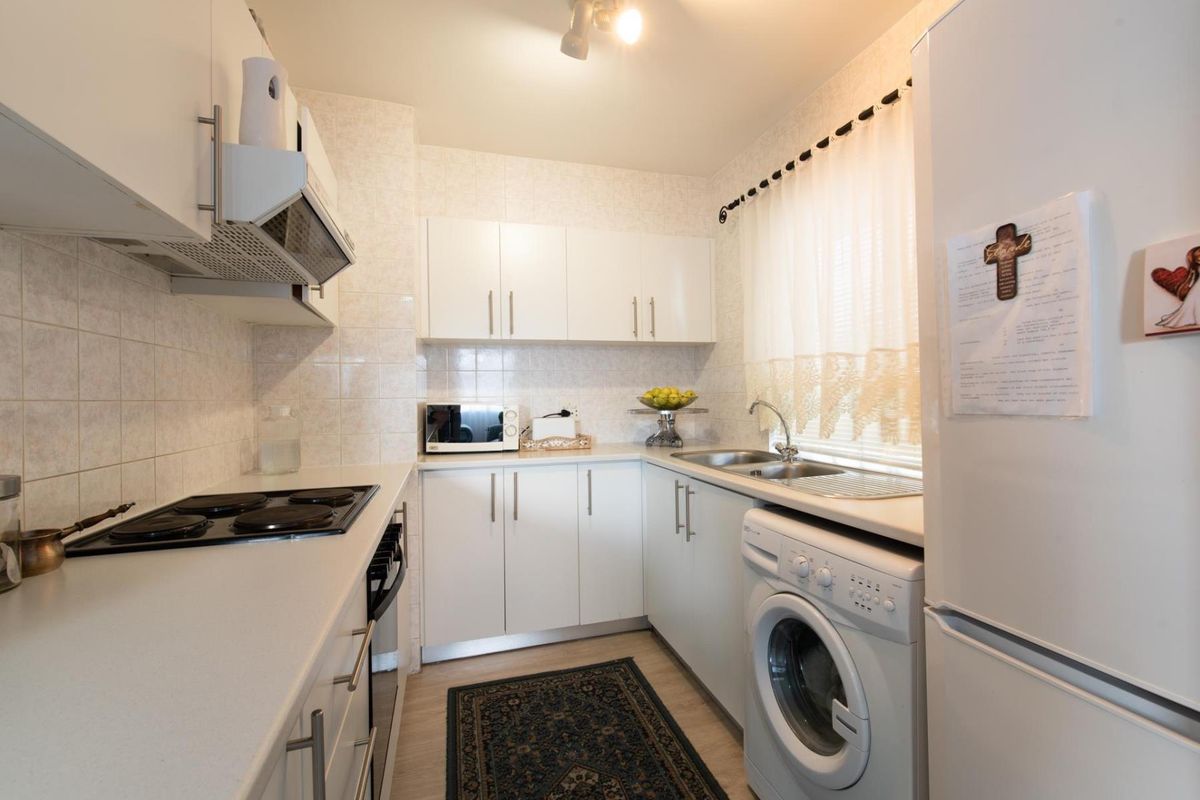 A functional galley-style kitchen featuring white cabinetry, tiled backsplash, integrated electric hob, oven, and dedicated space for laundry appliances.