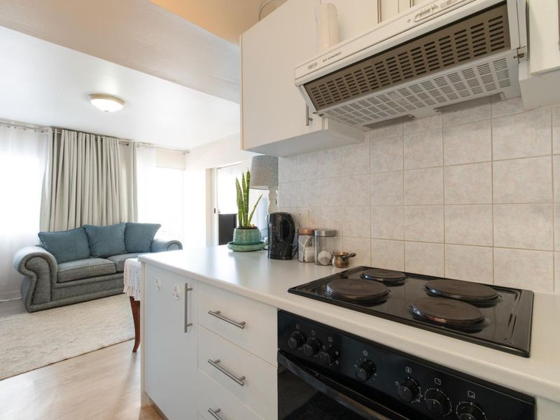 Open-plan kitchen and living area featuring white cabinetry, electric cooking appliances, tiled backsplash, and light-toned laminate flooring.