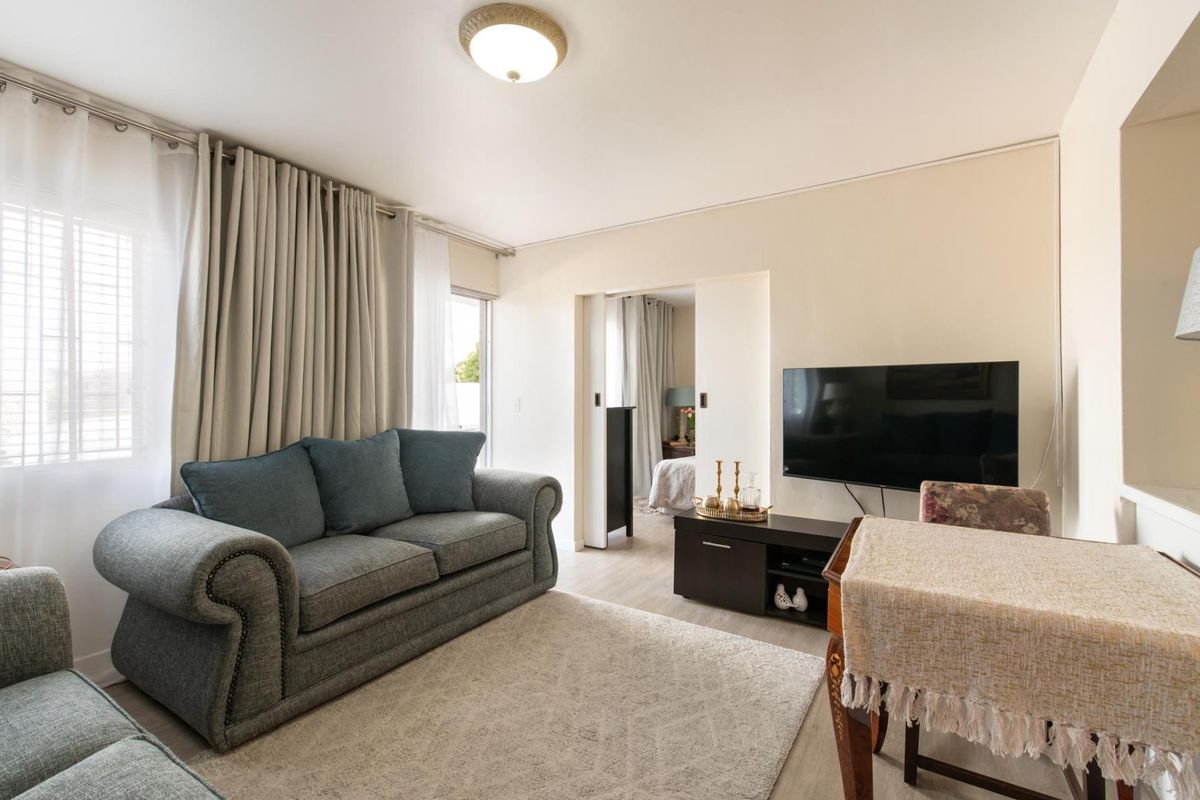 A well-lit living room featuring neutral walls, laminate flooring, and a sliding door providing access to an adjacent bedroom.