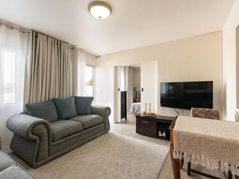 A well-lit living room featuring neutral walls, laminate flooring, and a sliding door providing access to an adjacent bedroom.