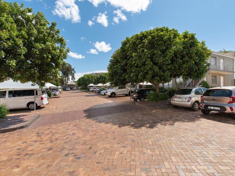 A well-maintained paved parking area for the apartment complex, featuring established trees and covered parking bays.