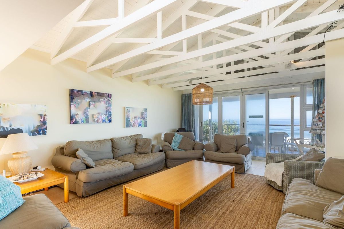 Spacious living room featuring a vaulted ceiling with exposed white timber rafters and large sliding glass doors offering ocean views.