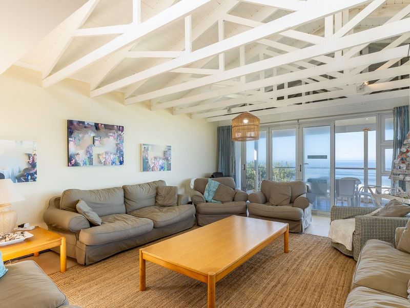 Spacious living room featuring a vaulted ceiling with exposed white timber rafters and large sliding glass doors offering ocean views.
