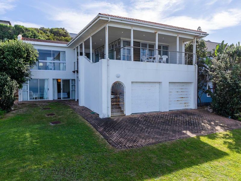 Rear view of the property featuring a double garage, a spacious covered balcony, and a paved driveway leading to a garden area.