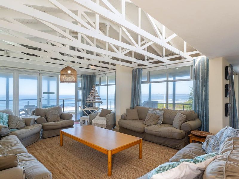 Spacious living room featuring high exposed white timber trusses, large windows, and sliding doors that offer expansive coastal views.