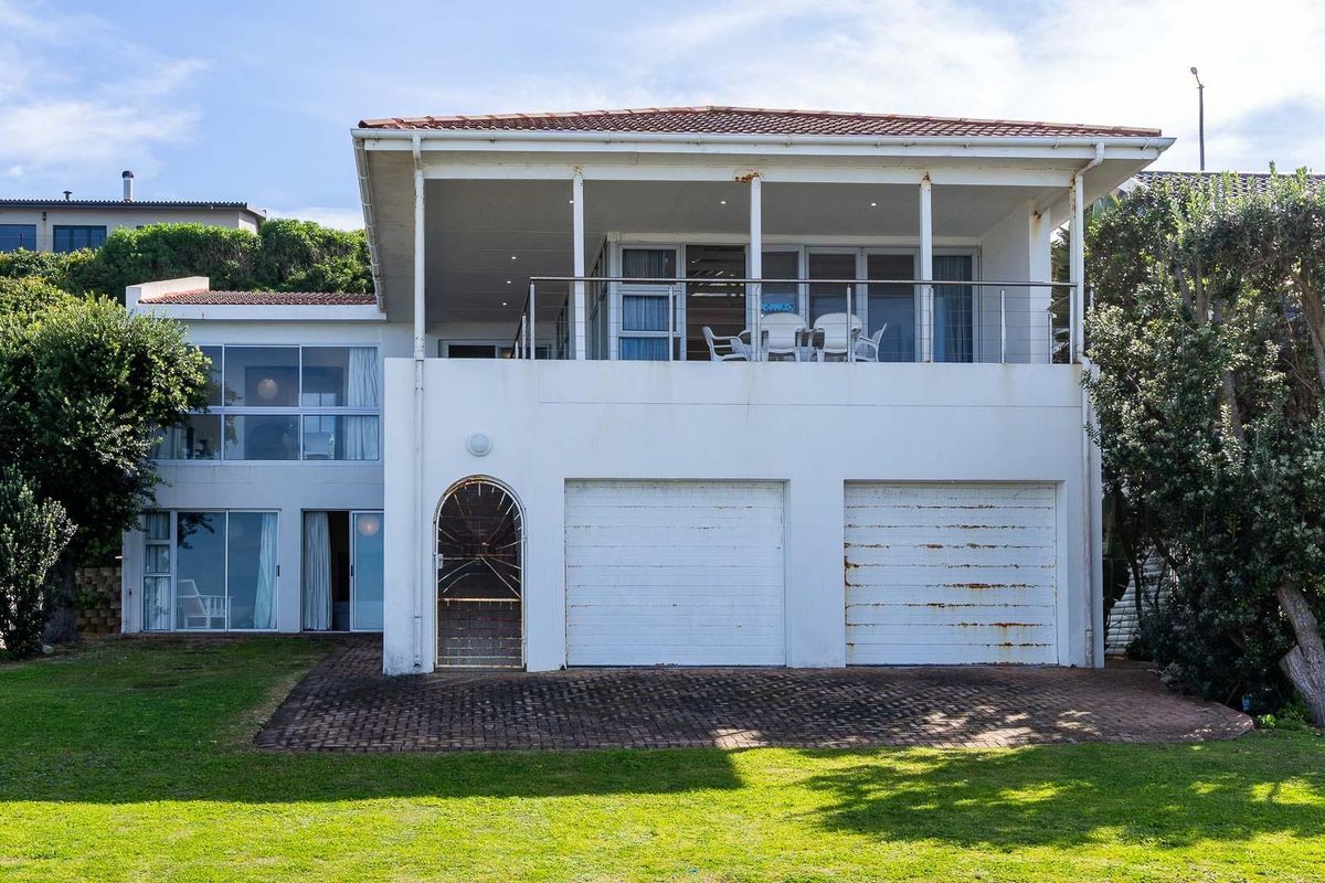 Rear view of a two-story house featuring a double garage, a spacious upper balcony, and a well-maintained lawn area.