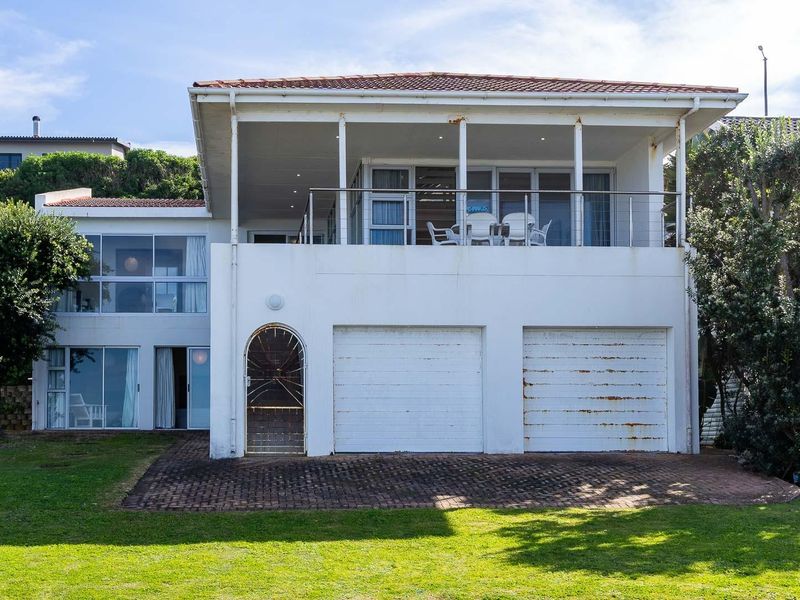 Rear view of a two-story house featuring a double garage, a spacious upper balcony, and a well-maintained lawn area.