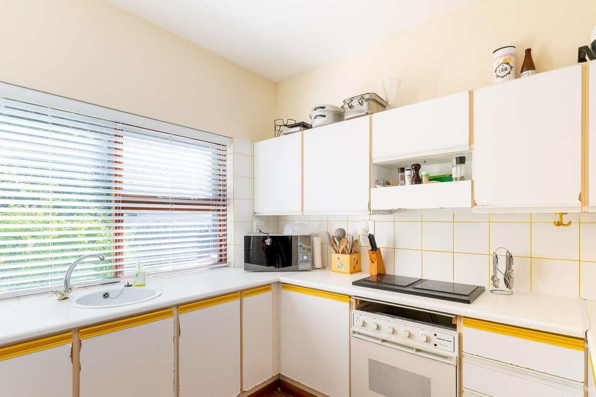 A functional kitchen featuring white built-in cabinetry, a tiled backsplash, a built-in oven with hob, and a large window with venetian blinds.